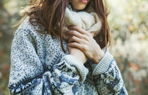 Person wearing sweater and scarf holds hands over heart one over the other. Top of face is cropped from photo