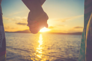 Photo of couple's entwined hands against background of sea and sunset