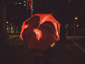 Silhouettes of couple about to kiss are visible behind a red umbrella