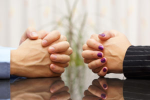 Cropped image of folded hands of two partners seated at opposite sides of table