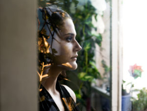 Leafy pattern from trees casts shadow over face of person looking out window