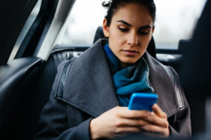 Upset person in business dress and scarf with ponytail texting in car as passenger
