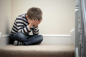 Child sits on stairs, covering face with both hands