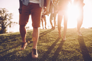 Close-up cropped photo of group of people walking along grassy area in early morning sunlight