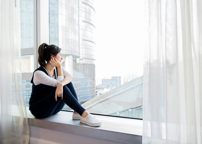 Woman looking out window thoughtfully, reflecting on her mental health