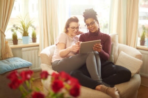 Couple sits together with legs crossed together using tablet and smiling