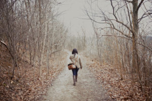 Rear view photo of young person in coat with bag and long hair out for a hike in late autumn
