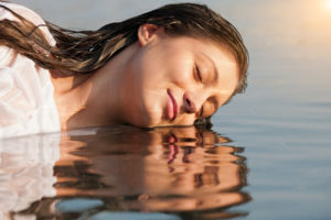 Smiling person with long hair rests face on water 