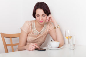 Person sitting in cafe looks at phone with bored or annoyed expression