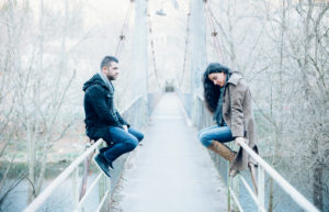 Young couple with relationship difficulties sitting on opposite sides of a bridge