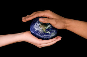One hand each from two different people reach out and support small globe model of Earth on black background