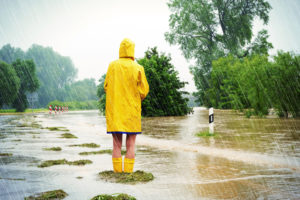 Rear view of person in yellow hooded raincoat standing on flooded street looking at the water as it rises
