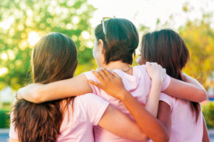 Three people with pink shirts embrace outdoors. Rear view photo