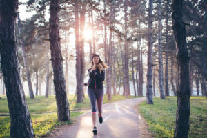 Person in athletic clothes with long hair wears hat and runs along forest track