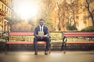 Person in business suit sits on park bench on autumn day looking at papers 