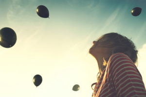 Girl looking up at black balloons in sky