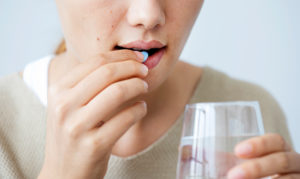 Close-up image of lower face of person taking a blue pill while holding a glass of water