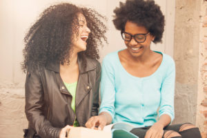 Two friends sit together and look at book, laughing happily