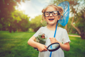 young school-age child with hair tied up wears glasses and explores with magnifying glass