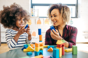 Preschooler and parent play blocks together. Both are smiling. 