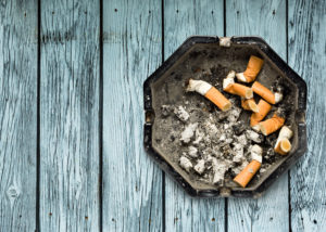 Ashtray of cigarette butts on light gray table