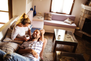 Loving couple cuddles on sofa smiling at each other while drinking coffee in living room