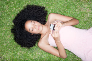 A teenage girl is lying on the grass with her phone.