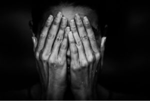 Black and white photo of person's hands covering their face
