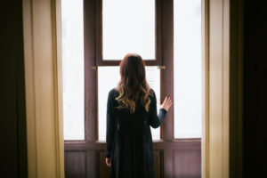 Rear view image of person in long dress staring out windowed doors