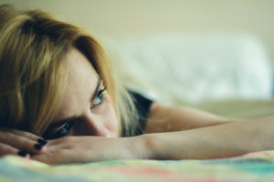 Close-up photo of person lying in bed resting face on hands looking to the side, not wanting to get up