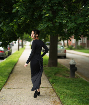 Person in long black dress walks down street looking back over shoulder