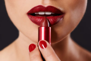 A woman applies crimson lipstick.