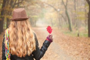 Rear view of person with long hair and hat holding red leaf