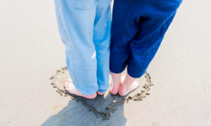 A couple stands together in a heart drawn in the sand.