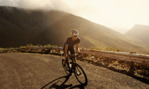 Person in helmet and cycling gear rides bike up hill at sunset