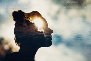 Double exposure image shows silhouette of person's head looking out among clouds with second exposure of clouds