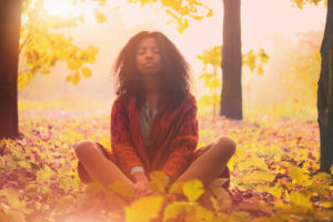 Young person with long hair sits on ground, eyes closed, calm expression on face