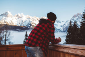 Standing in front of house and enjoying in winter day with cup of hot drink. Mountains in background are coverd with snow.