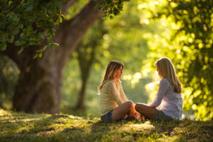 Mom and daughter sitting on a grass in the park and talking.