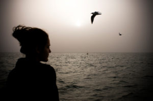 A sad woman watches seagulls in the fog.