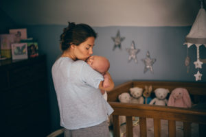 Woman kissing baby goodnight in nursery next to crib