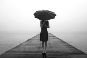 A woman in a black dress hides her face with her umbrella.