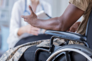 A veteran in a wheelchair speaks to a doctor in the background.
