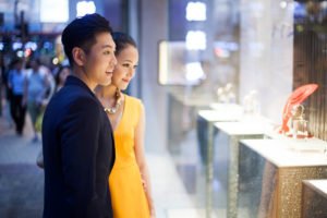 A young couple admires a necklace through the shop window.