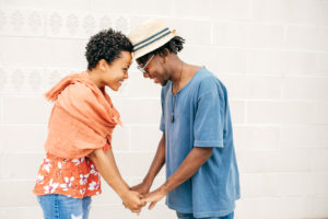 Couple standing a few paces apart face each other, holding hands and smiling
