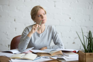 Person sits at desk, pen held to mouth, looking thoughtful, as if forgetting something