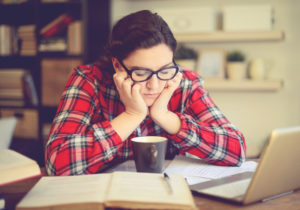 Person sitting at kitchen table with head in hands while working, frustrated expression