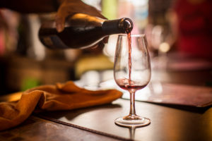 Close-up photo of warmly lit room. Red wine is being poured into wineglass by person's hand