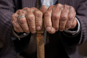 A close-up of two wrinkled hands holding a cane.