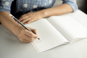 A woman writes in a notebook with her pencil.